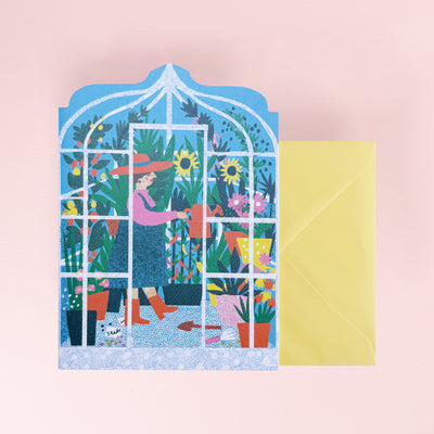 Greeting card with a colorful illustration of a woman in a garden, featuring a yellow envelope on a pink background.