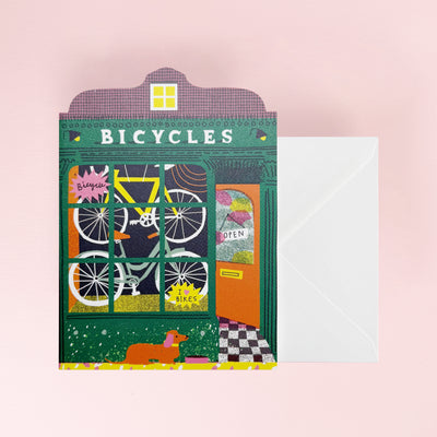 Card with bicycle-themed design and envelope on a pink background
